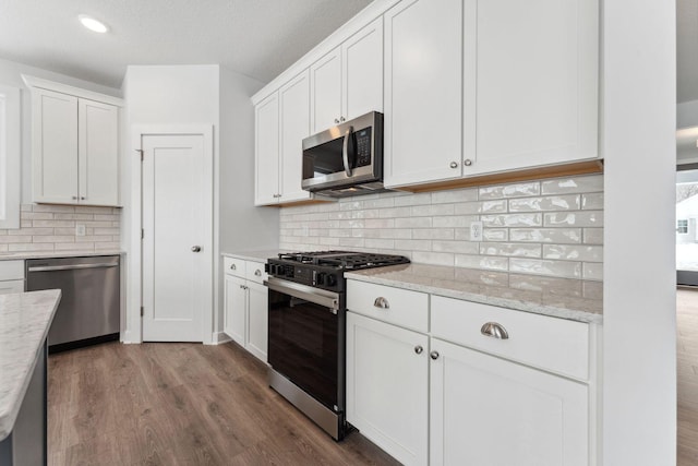 kitchen with stainless steel appliances, white cabinetry, wood-type flooring, and light stone counters