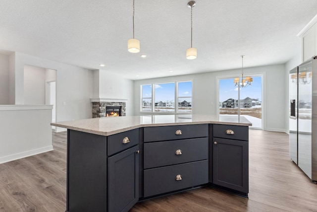 kitchen with white cabinetry, decorative light fixtures, a center island, stainless steel fridge, and hardwood / wood-style floors