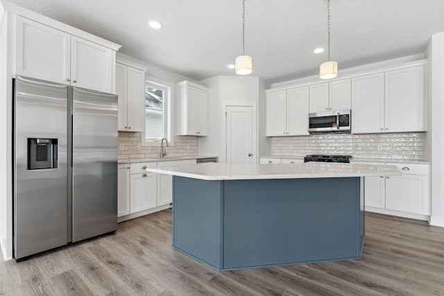 kitchen featuring stainless steel appliances, a center island, white cabinets, and decorative light fixtures