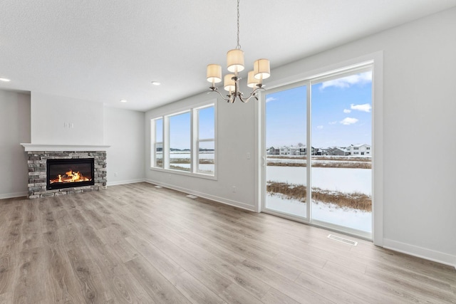 unfurnished living room with light wood-type flooring, a chandelier, a textured ceiling, and a fireplace