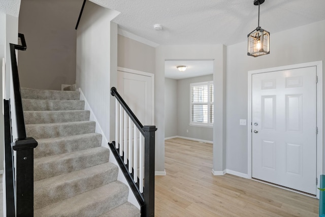 entryway with a textured ceiling, stairs, light wood-style flooring, and baseboards