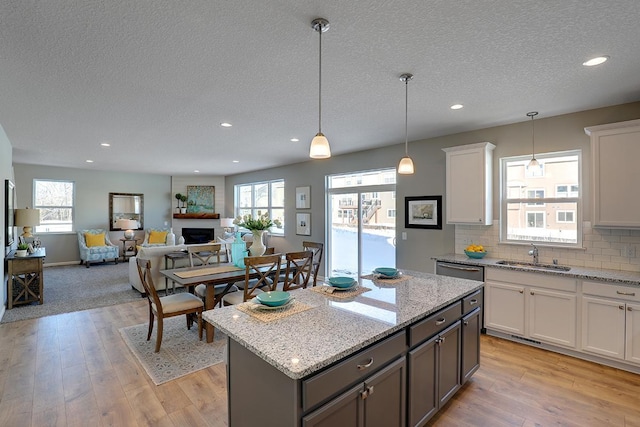 kitchen featuring hanging light fixtures, light stone countertops, white cabinets, a center island, and sink