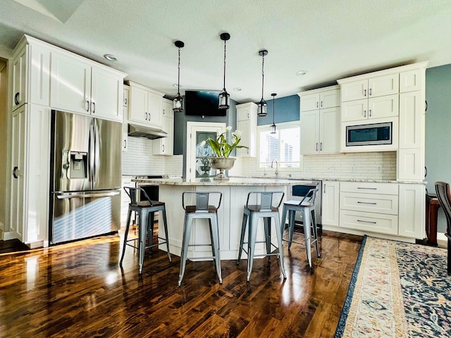 kitchen with pendant lighting, white cabinets, a center island, stainless steel appliances, and dark hardwood / wood-style floors