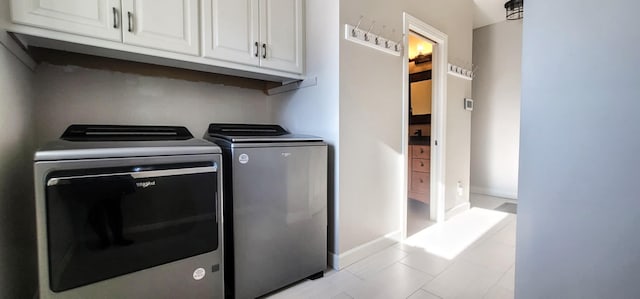 clothes washing area featuring washing machine and dryer, cabinets, and light tile patterned flooring