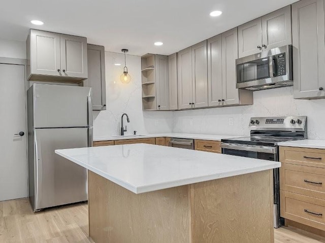 kitchen with appliances with stainless steel finishes, sink, hanging light fixtures, light stone counters, and light hardwood / wood-style flooring