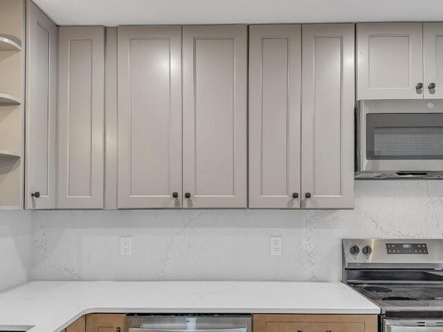 kitchen featuring tasteful backsplash, stainless steel appliances, light stone countertops, and gray cabinetry