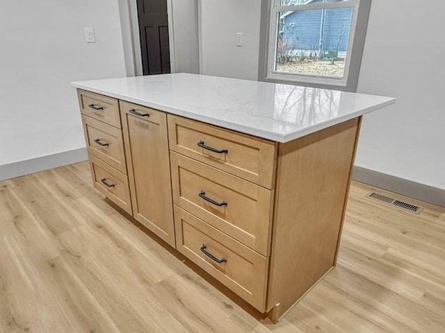 kitchen featuring light stone countertops, a center island, light brown cabinetry, and light hardwood / wood-style flooring