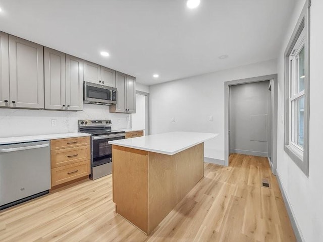 kitchen featuring a kitchen island, gray cabinetry, backsplash, light hardwood / wood-style floors, and stainless steel appliances