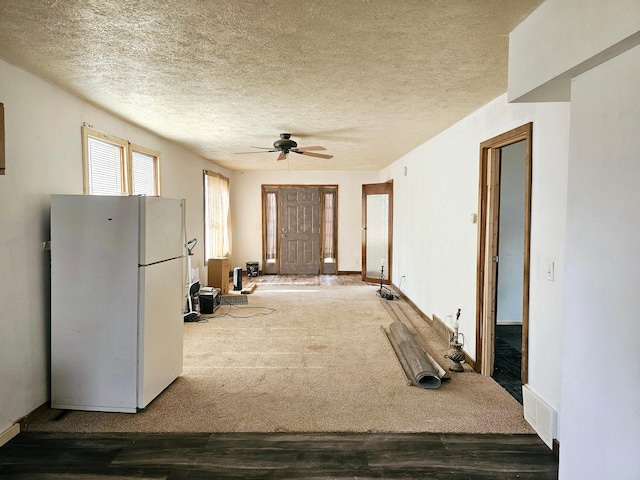 interior space featuring carpet floors, a ceiling fan, freestanding refrigerator, and a textured ceiling