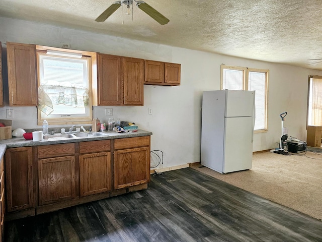 kitchen featuring a sink, ceiling fan, brown cabinets, freestanding refrigerator, and dark wood-style flooring