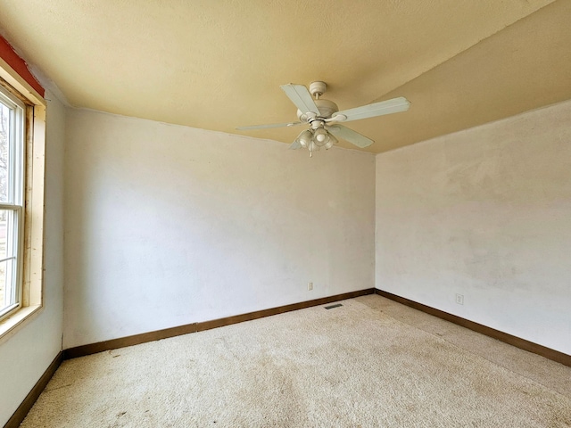 spare room with a wealth of natural light, carpet flooring, a ceiling fan, and baseboards