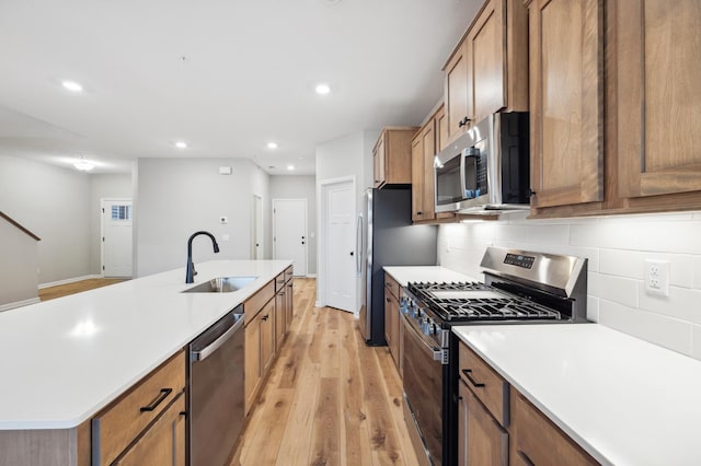 kitchen featuring sink, decorative backsplash, stainless steel appliances, a center island with sink, and light hardwood / wood-style flooring