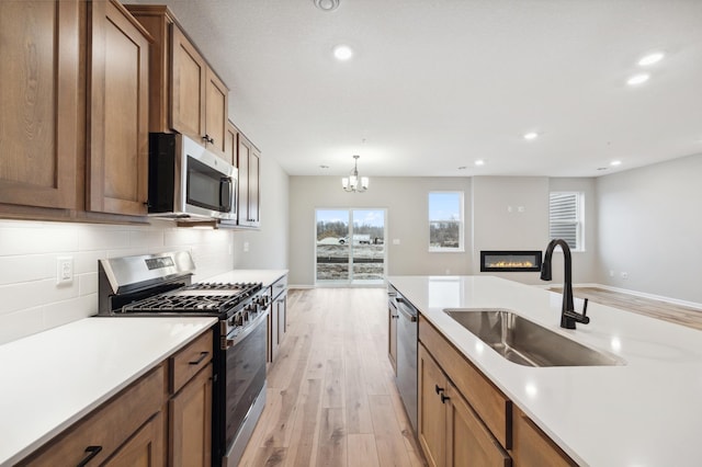 kitchen with appliances with stainless steel finishes, tasteful backsplash, sink, hanging light fixtures, and light hardwood / wood-style floors