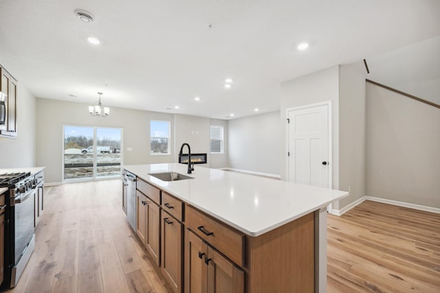 kitchen with pendant lighting, sink, stainless steel appliances, light hardwood / wood-style floors, and a center island with sink