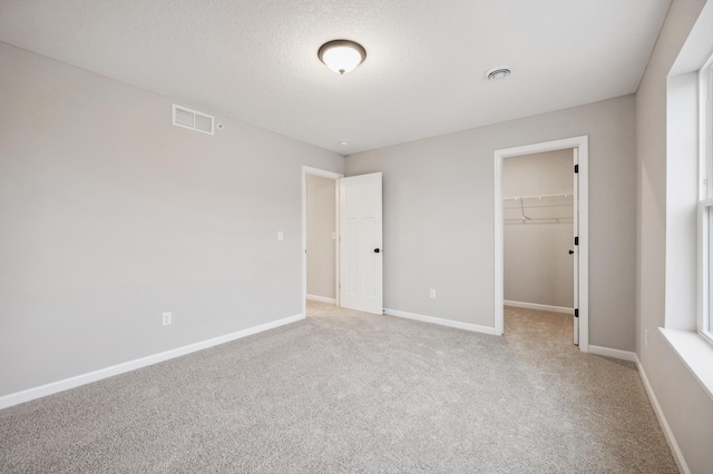 unfurnished bedroom featuring a walk in closet, light colored carpet, a closet, and a textured ceiling