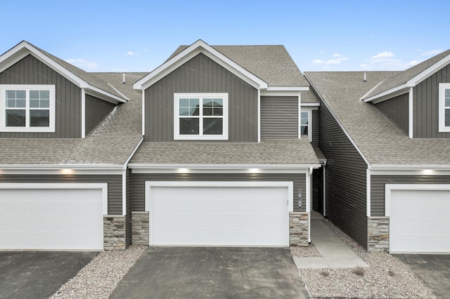 view of property featuring a garage, driveway, roof with shingles, and stone siding