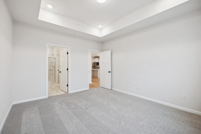 unfurnished bedroom with connected bathroom, a raised ceiling, and light carpet