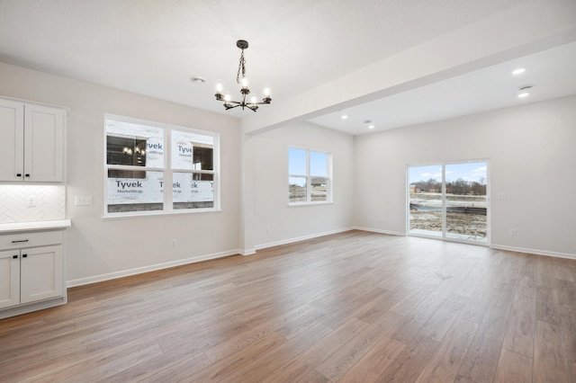 unfurnished dining area featuring a wealth of natural light, a notable chandelier, light wood finished floors, and baseboards