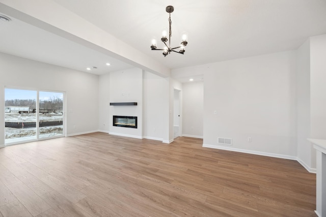 unfurnished living room featuring a glass covered fireplace, baseboards, visible vents, and light wood-type flooring