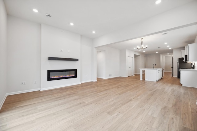 unfurnished living room with recessed lighting, a glass covered fireplace, a chandelier, and light wood finished floors