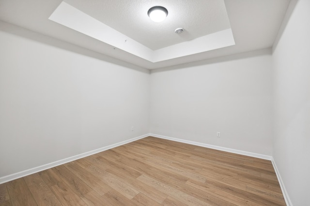 unfurnished room with a tray ceiling, a skylight, light wood-type flooring, and baseboards