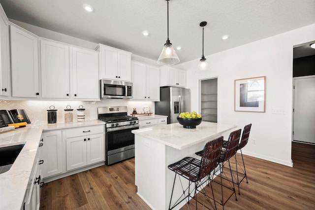 kitchen featuring white cabinetry, appliances with stainless steel finishes, a center island, and decorative light fixtures