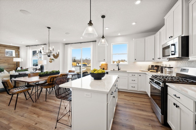 kitchen featuring stainless steel appliances, white cabinetry, hanging light fixtures, and a center island