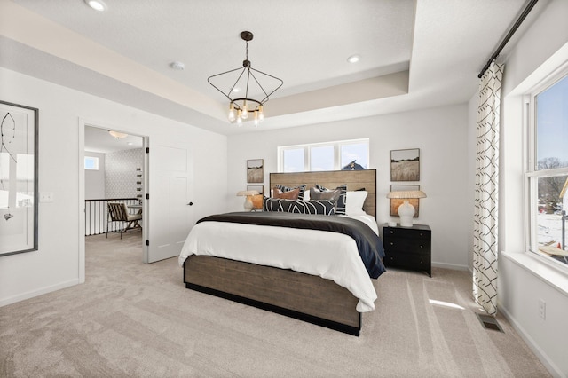 carpeted bedroom with a raised ceiling and a notable chandelier