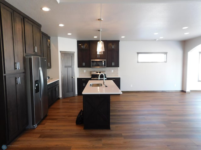 kitchen with sink, dark hardwood / wood-style floors, pendant lighting, stainless steel appliances, and a kitchen island with sink