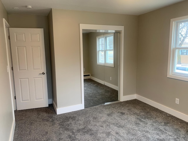 unfurnished bedroom with a closet, dark carpet, and baseboard heating