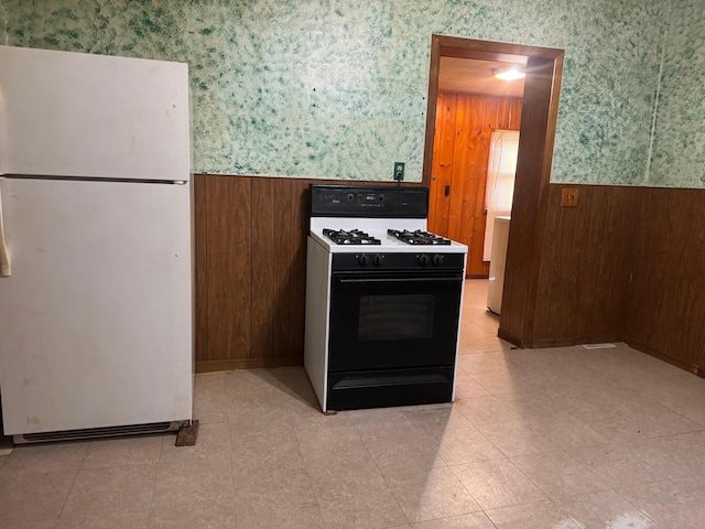 kitchen with white fridge, gas stove, and wood walls