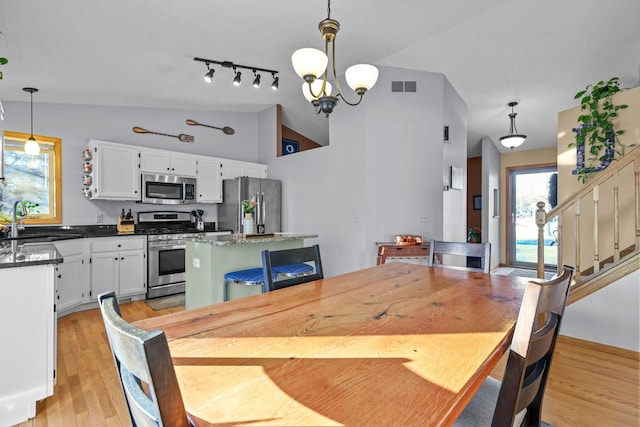 dining space with sink, rail lighting, a notable chandelier, light hardwood / wood-style floors, and vaulted ceiling