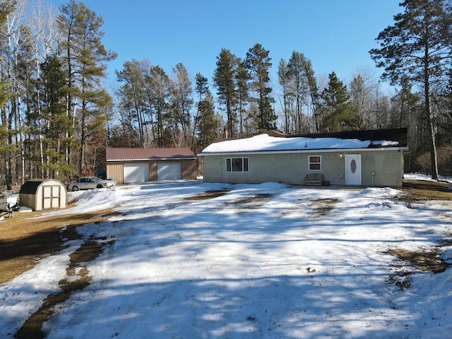 snow covered property featuring a garage, an outdoor structure, and a shed