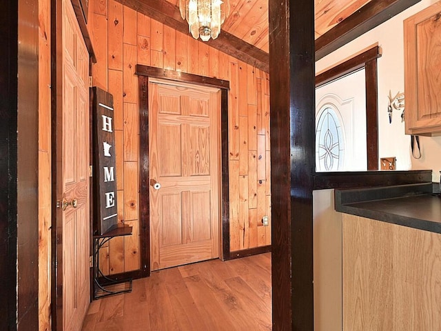 kitchen with light wood-style floors, wooden walls, dark countertops, and an inviting chandelier