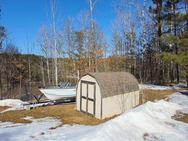 snow covered structure with a storage shed, an outdoor structure, and a wooded view