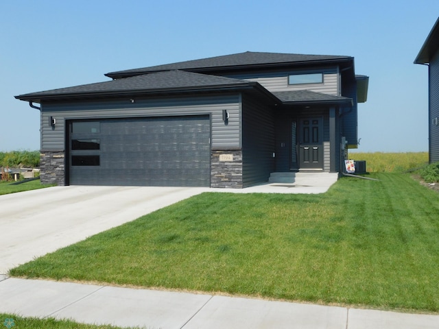 prairie-style house with a garage, stone siding, driveway, and a front yard