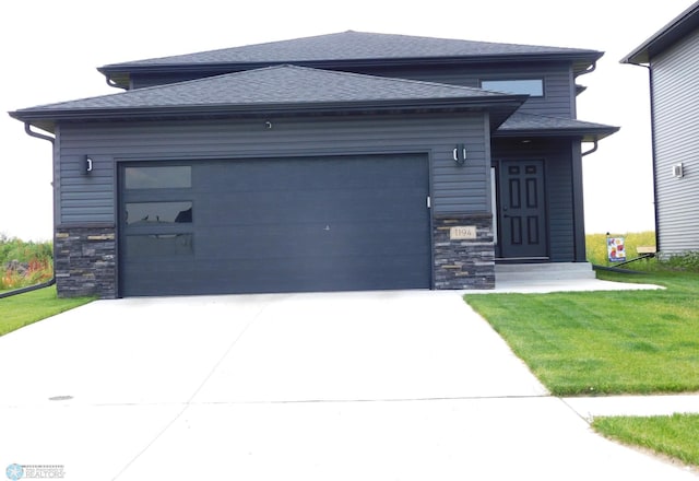 prairie-style house with a front yard, an attached garage, and stone siding