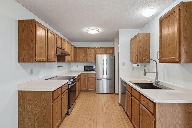 kitchen featuring sink, light hardwood / wood-style floors, a textured ceiling, and appliances with stainless steel finishes