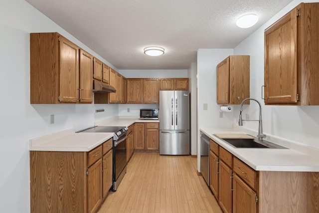 kitchen featuring under cabinet range hood, brown cabinetry, appliances with stainless steel finishes, and a textured ceiling