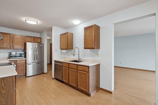 kitchen with stainless steel appliances, light wood-style flooring, a sink, and brown cabinetry