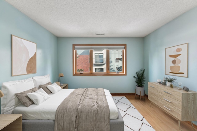 bedroom with baseboards, visible vents, a textured ceiling, and light wood-style floors