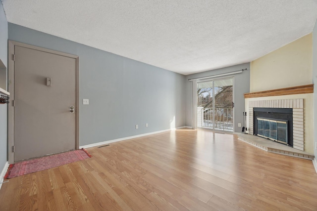 unfurnished living room featuring a brick fireplace, a textured ceiling, and light hardwood / wood-style floors