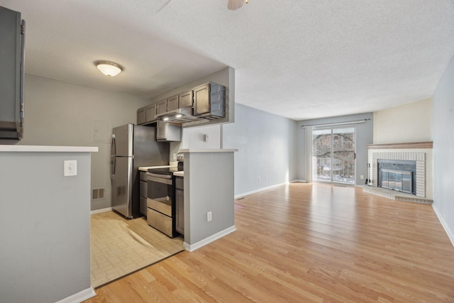 kitchen featuring a textured ceiling, a brick fireplace, stainless steel appliances, and light hardwood / wood-style flooring