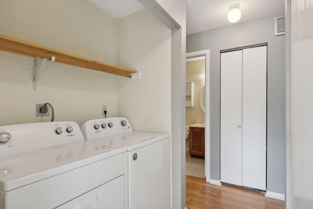 clothes washing area with washer and clothes dryer, a textured ceiling, and light hardwood / wood-style floors