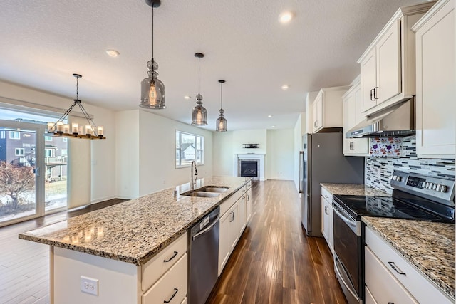 kitchen with white cabinetry, sink, hanging light fixtures, stainless steel appliances, and a center island with sink