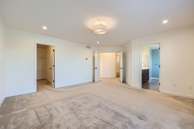 unfurnished bedroom with light colored carpet, ensuite bathroom, a spacious closet, and a closet