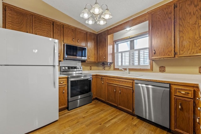 kitchen with sink, vaulted ceiling, hanging light fixtures, light wood-type flooring, and stainless steel appliances