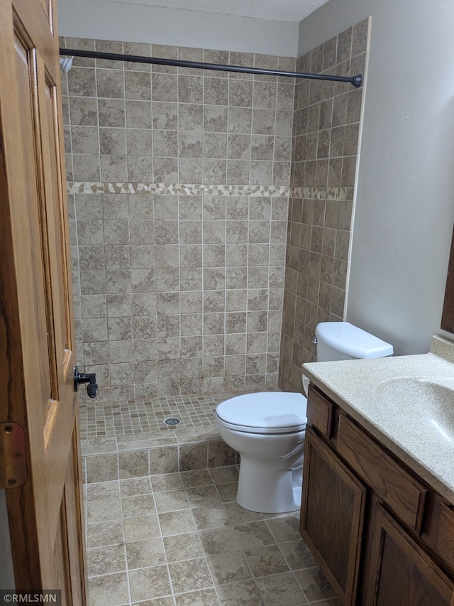 bathroom featuring toilet, vanity, and a tile shower