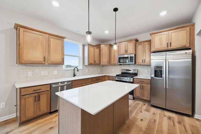 kitchen with sink, decorative light fixtures, appliances with stainless steel finishes, a kitchen island, and light hardwood / wood-style floors