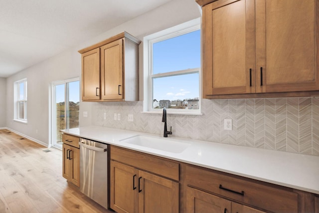 kitchen featuring a healthy amount of sunlight, sink, dishwasher, and light wood-type flooring